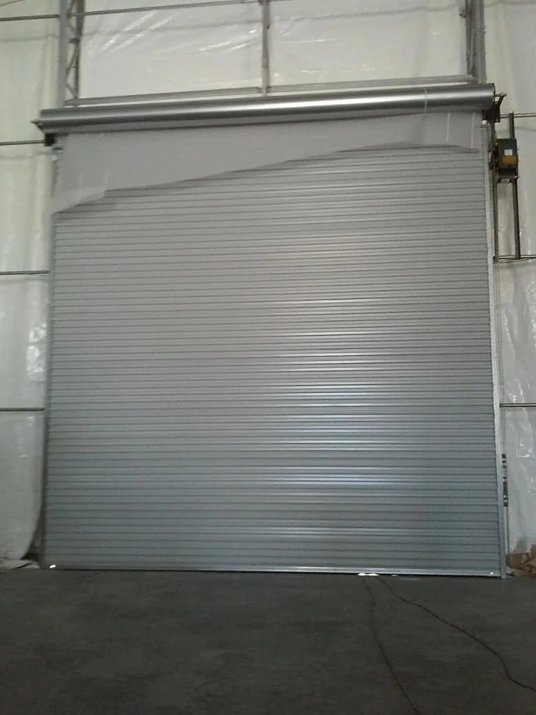Grey roll-up door inside a large facility with a translucent roof