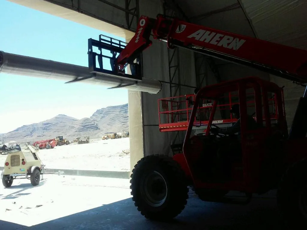 Telehandler under a wide warehouse opening, desert mountains beyond