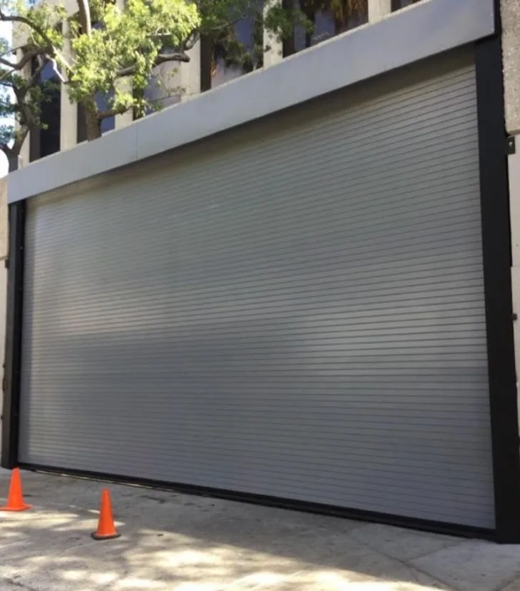 Wide rolling steel shutter across a storefront, traffic cones in front