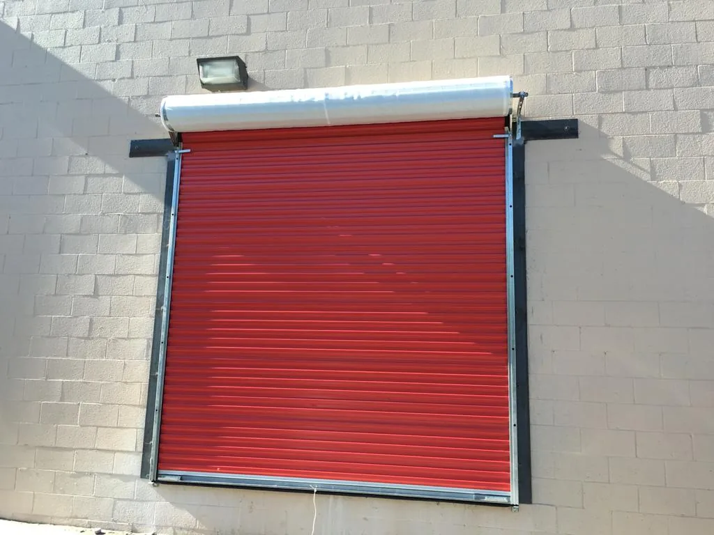 Red roll-up door mounted on a painted block wall under a flood light