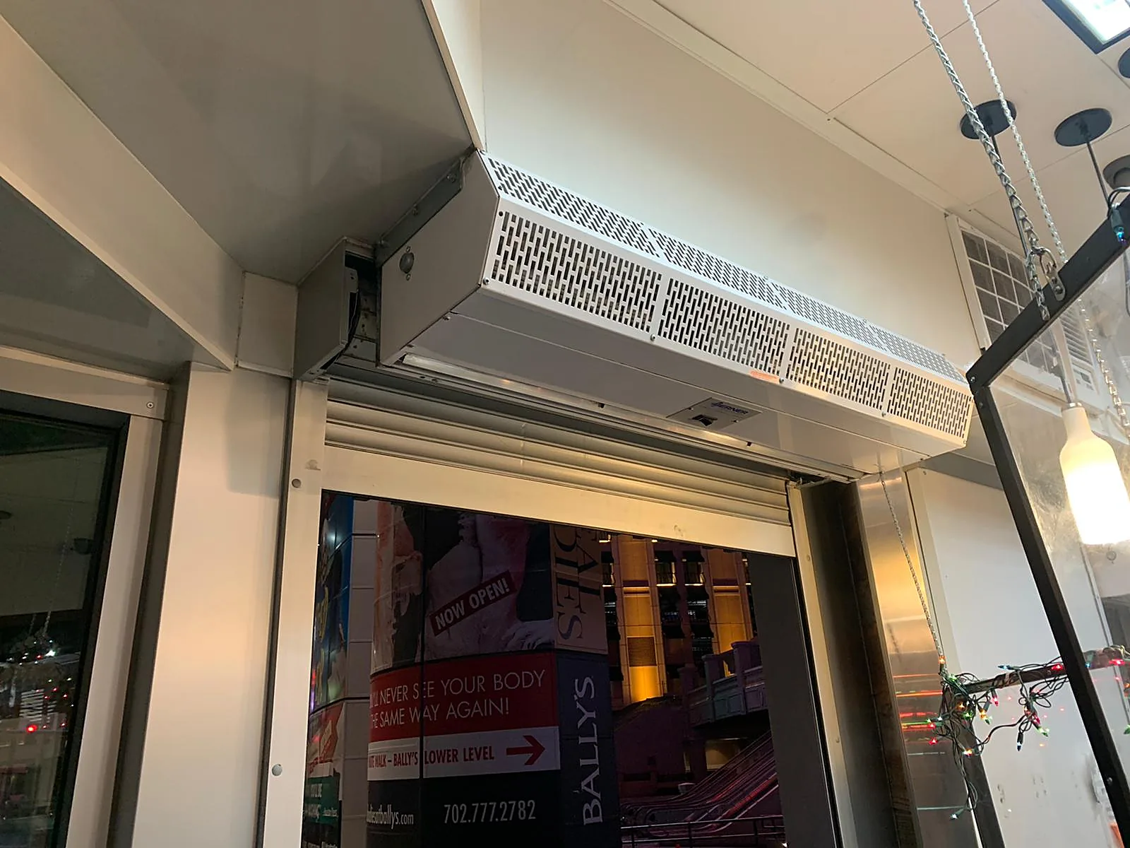 Storefront roll-up door and overhead air curtain at a shop entrance, with Bally's signage in the corridor beyond